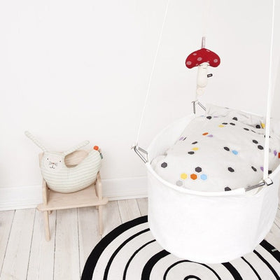 Scandinavian inspired nursery with swinging crib and rabbit peter cushion on a wooden chair.