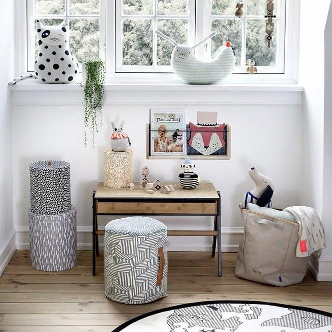 A bright and airy childrens room with lots of stylish and design led accessories under a window.  Draped over a storage basket you can see the smilla plaid blanket in off white grey colourway