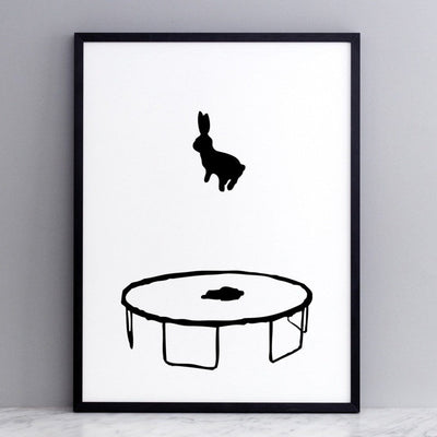 black and white image of HAM rabbit bouncing and playing on his trampoline.  Fun and playful series of prints.  Ideal for adults and children. Pictured here on marble surface with grey painted wall backdrop.